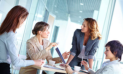 four women in business attire talking around a table